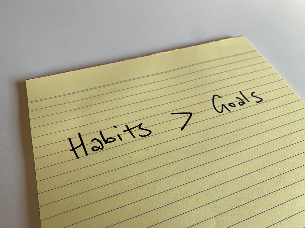 A notepad with handwritten "habits > goals" meaning habits are better than goals