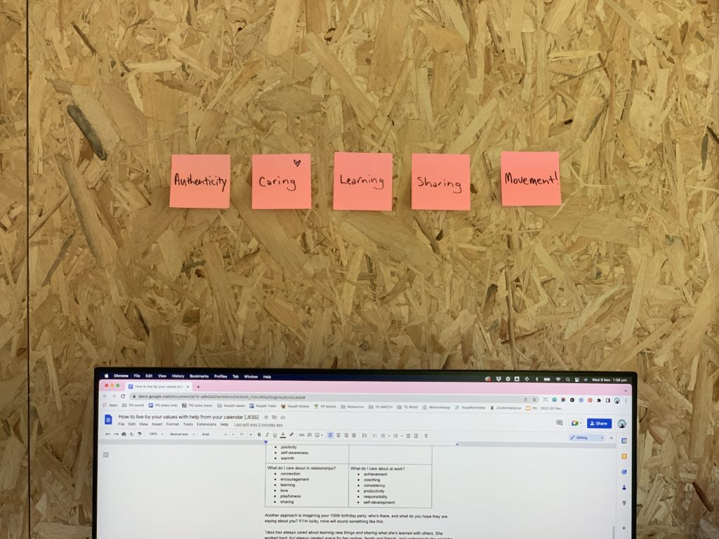 A photo of post it notes above a computer screen which read authenticity, caring, learning, sharing and movement