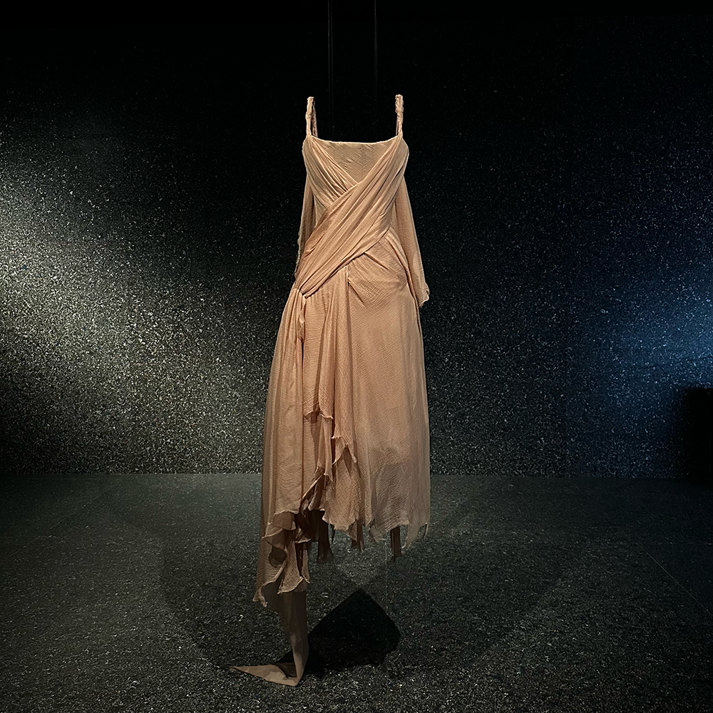 A beige, draped, strappy Alexander McQueen dress on display at a gallery