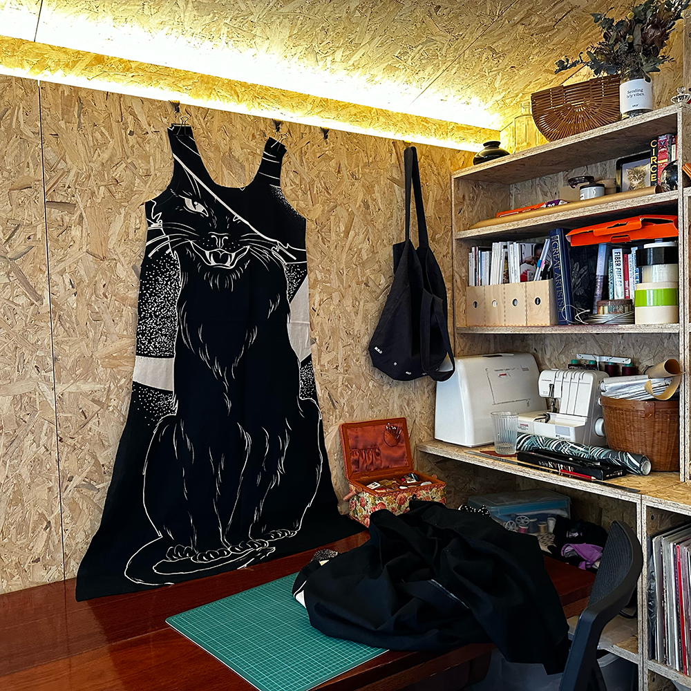 A sewing nook with a dress on the wall that has a witchy black cat print